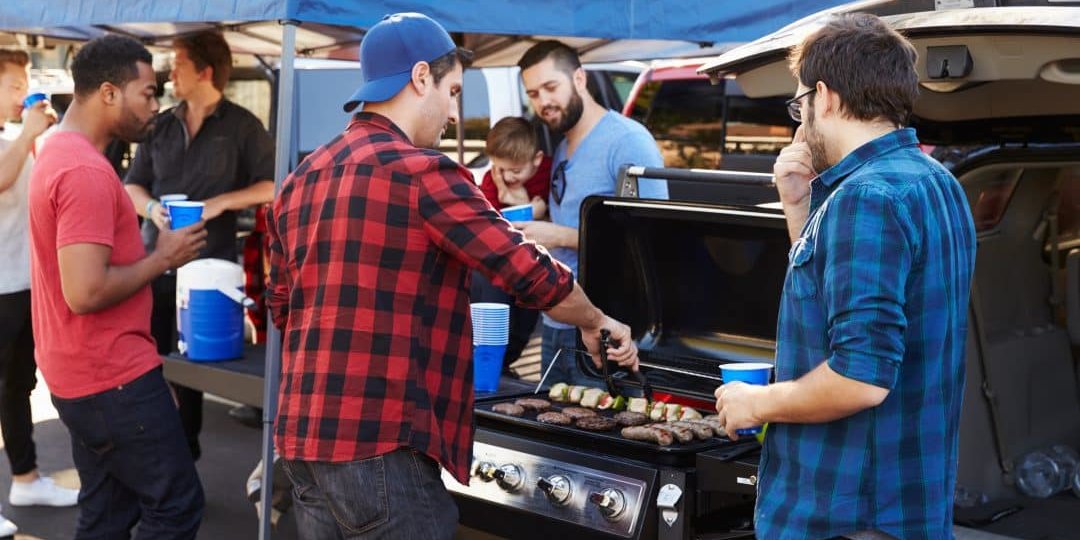 group of people cooking on a grill at an outdoor tailgate event